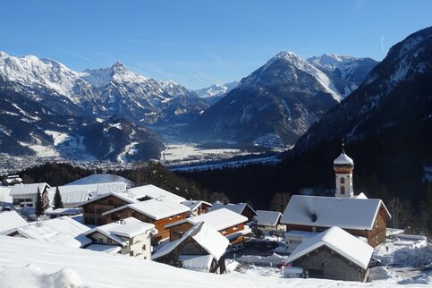 Bürserberg, auf dem Weg herauf. Foto: Melanie Fleisch / Alpenregion Bludenz Tourismus Verschneite Häuser und Kirche von Bürserberg, dahinter das Tal und die Berge
