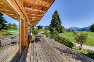 Die überdachte Terrasse Überdachte Holzterrasse von Chalet 1 mit Bank und Tisch, Blick über die Wiese zu den Bergen